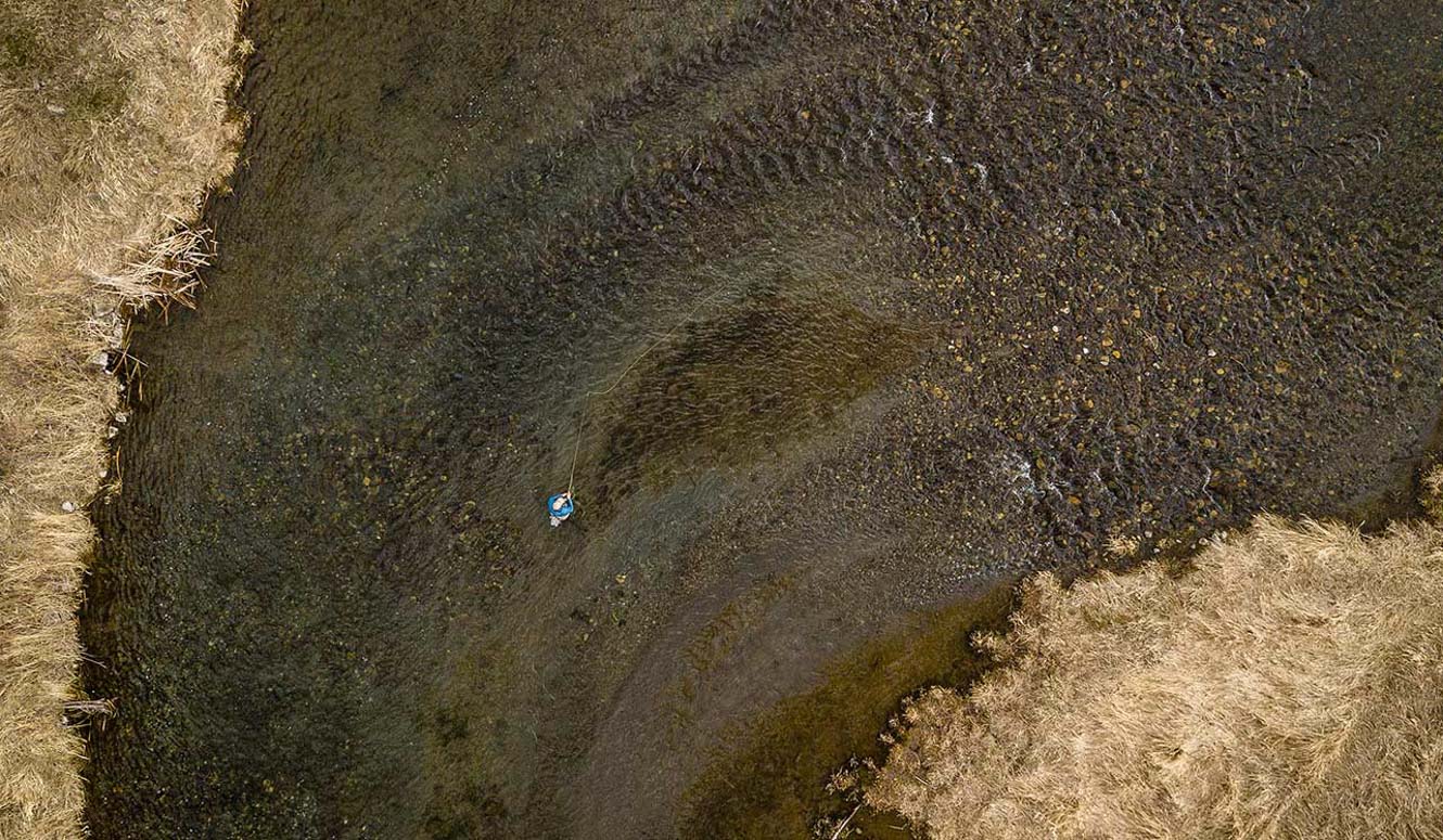 Overhead aerial view of a person fly fishing in a clear river.