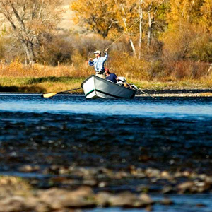 Fly fisherman in a drift boat on a river on a sunny fall day.