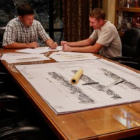 Two men sitting at a conference table reviewing building plans.