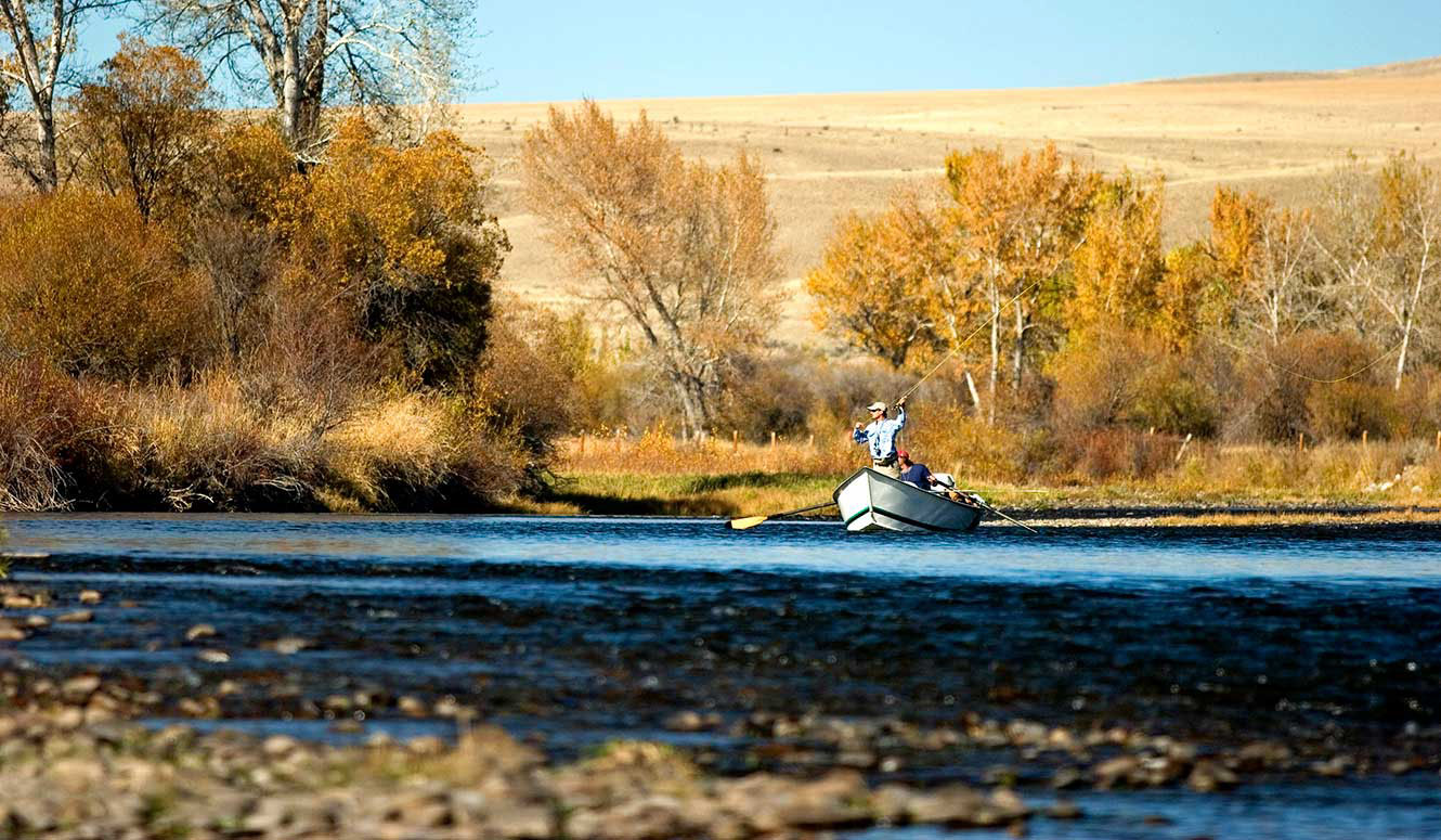 A man fly fishing from a drift boat on a sunny autumn day