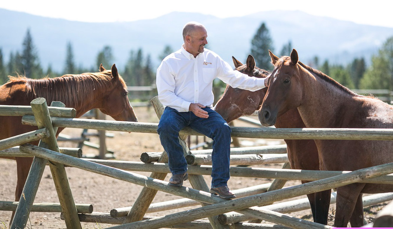 Man sitting on buck rail fence petting a horse in Big Sky, Montana