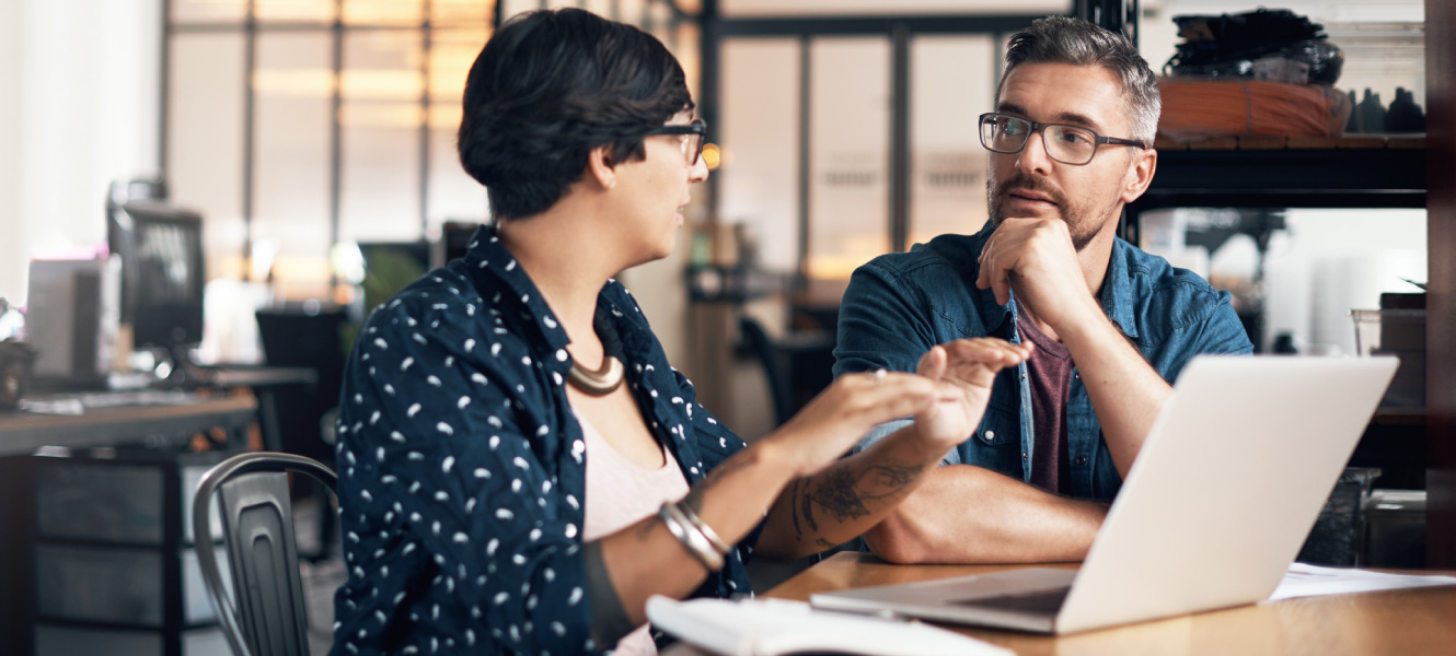 A man and woman having a discussion at a table with a laptop in front of them.