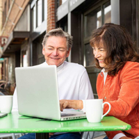 A couple sitting at an outside cafe working on a laptop.