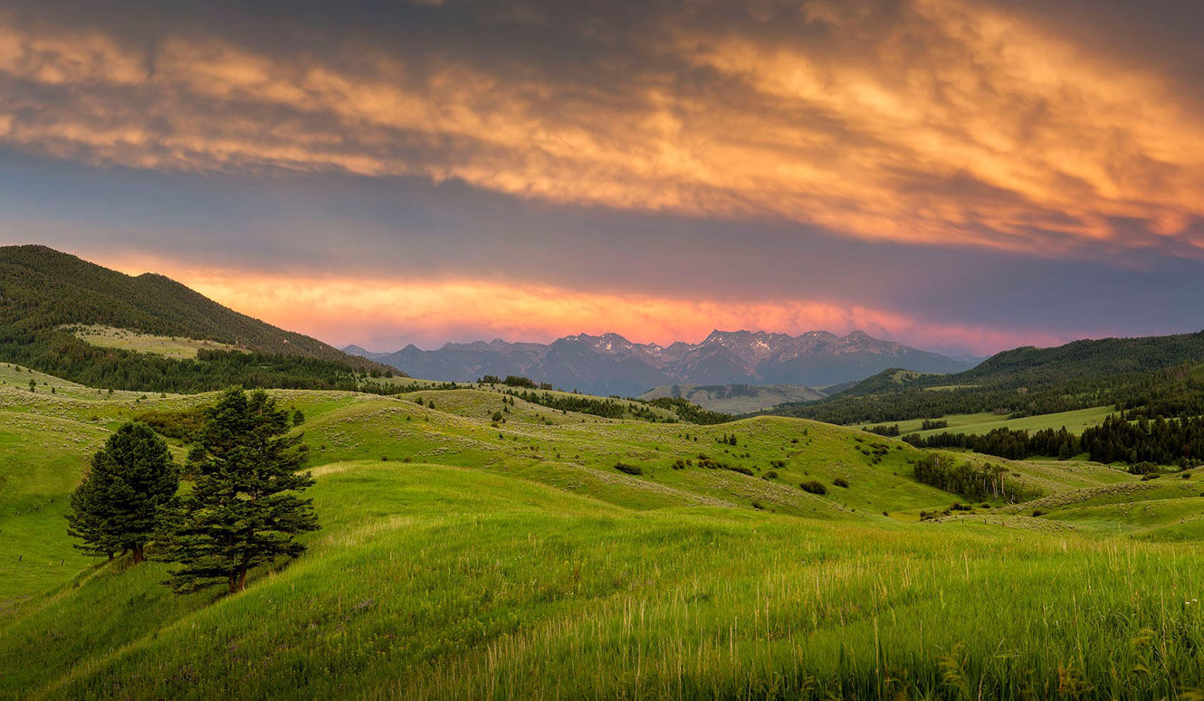 Sun setting over distant mountains with rolling green hills in the foreground.