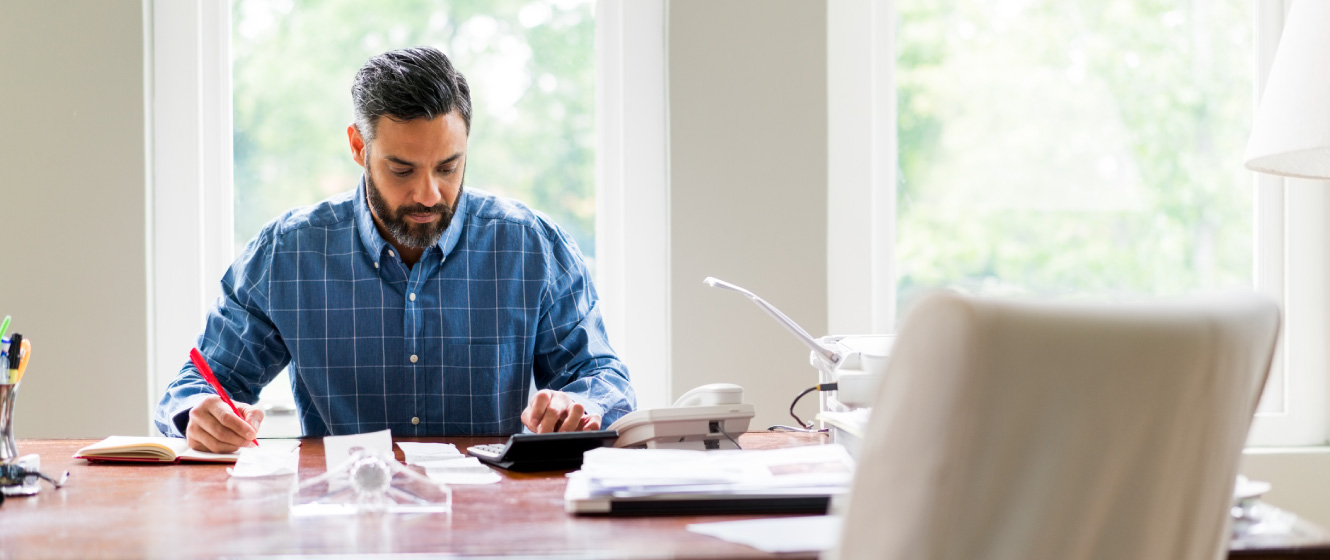 A man working at a table in his home. He's typing on a calculator.