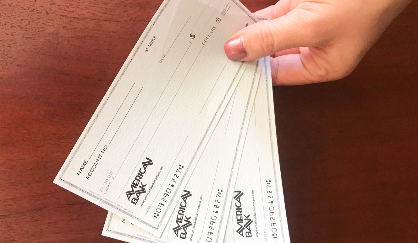 A person's hand holding blank sample checks above a wood desk.