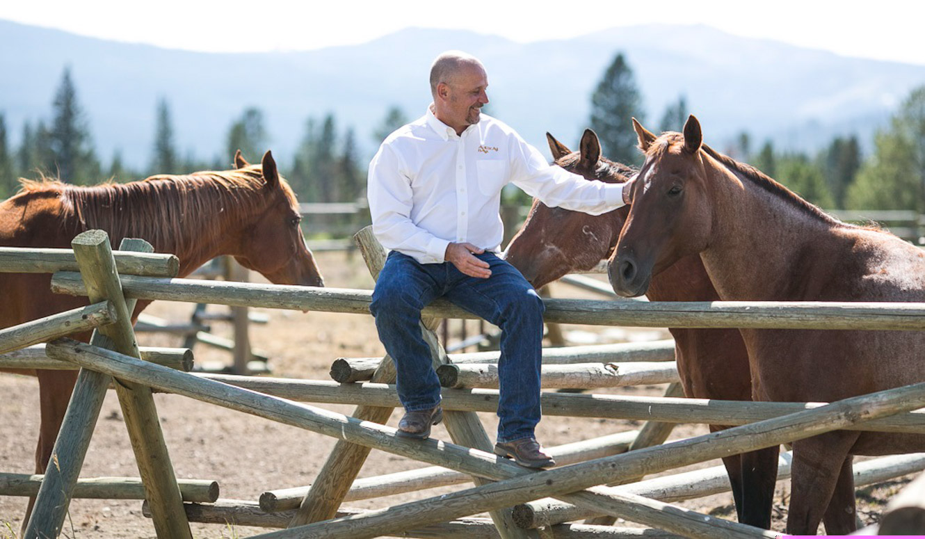 Man sitting on buck rail fence petting a horse in Big Sky, Montana